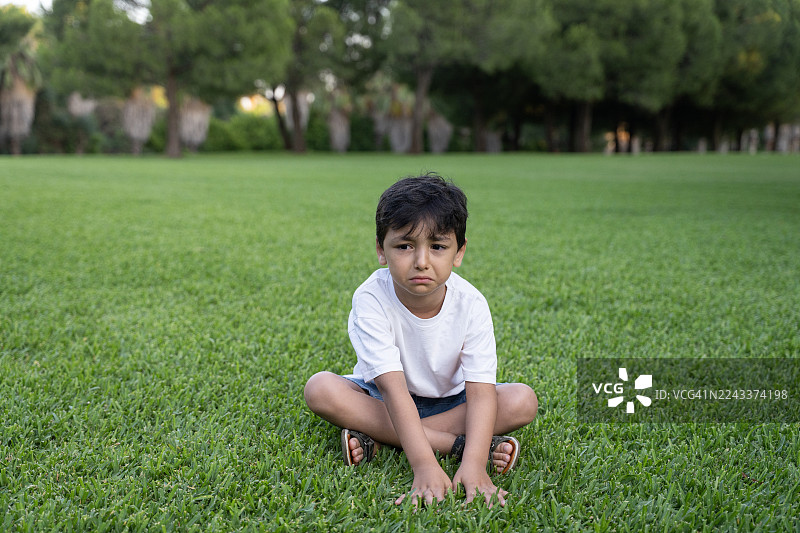 伤心的小男孩坐在公园的草地上图片素材