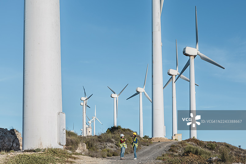 在西班牙阿尔梅里亚的风电场，两位女士在晴朗的蓝天下携手合作图片素材