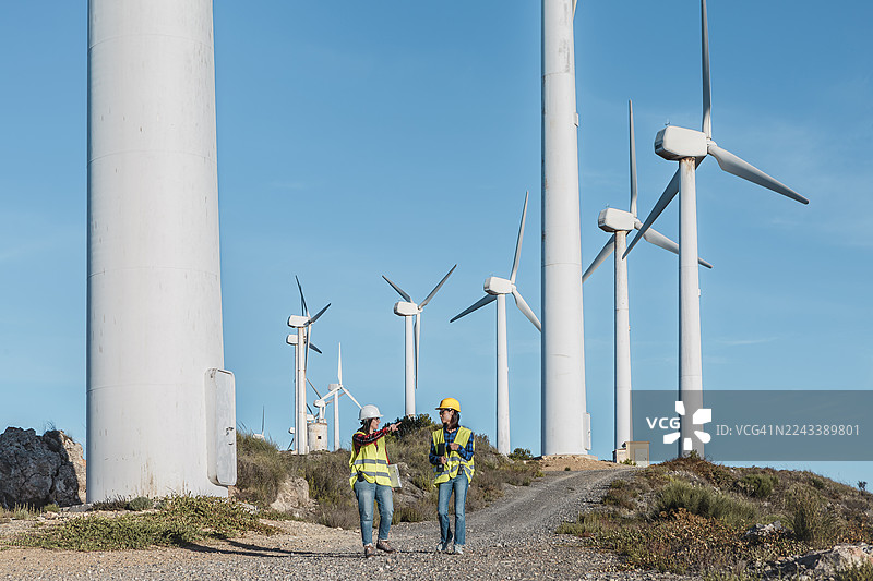 在西班牙阿尔梅里亚的风电场，两位女性正在合作，讨论可再生能源解决方案。图片素材