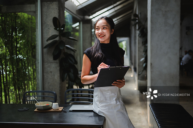 年轻的亚裔女服务员面带微笑，在一家现代餐厅工作，用剪贴板记录顾客订单图片素材