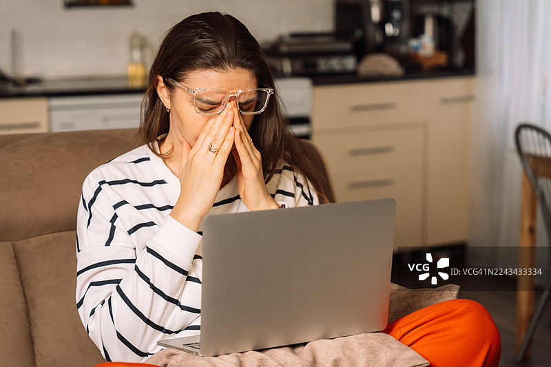 女子坐在沙发上，揉着眼睛，面前放着笔记本电脑图片素材