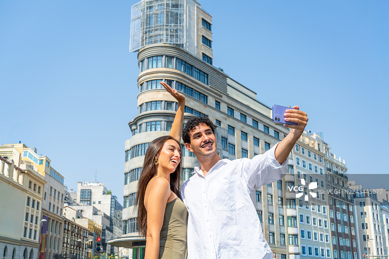 一对年轻的网红情侣在马德里享受夏日假期，背景是格兰大道上标志性的卡亚俄广场，他们正在自拍。西班牙马德里图片素材