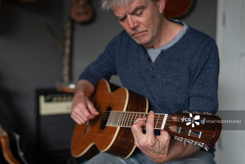 男人在家庭音乐室弹奏带有横按的声学吉他图片素材