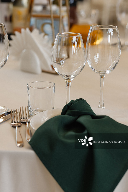 在优雅的宴会厅环境中，摆放着酒杯、餐具和绿色餐巾的餐桌布置图片素材