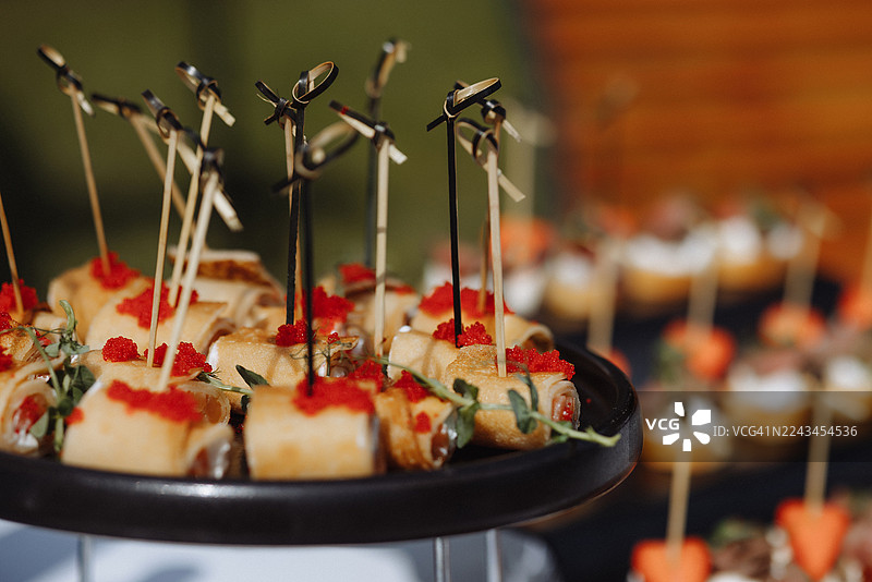 户外活动餐饮布置中，黑色托盘上的红鱼子酱可丽饼卷开胃菜图片素材
