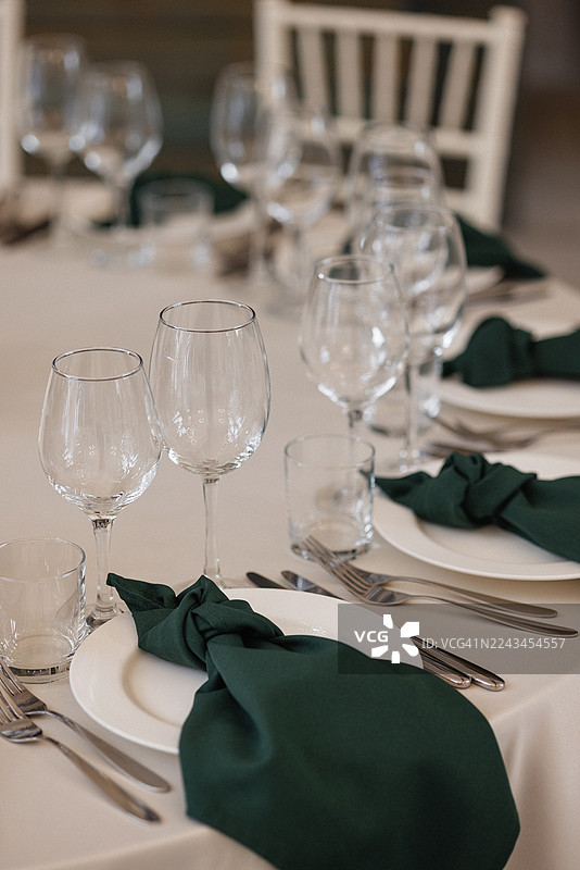 婚礼接待大厅里，优雅的宴会餐桌布置，配有酒杯、盘子和深绿色餐巾图片素材