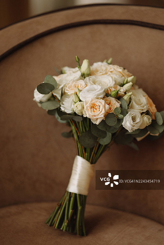 棕色软包椅子上的白色和淡粉色玫瑰与桉树组成的婚礼花束图片素材