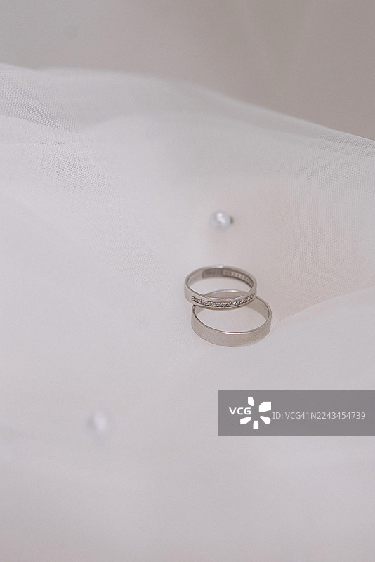 银色结婚对戒放在白色薄纱面料上，背景简约图片素材