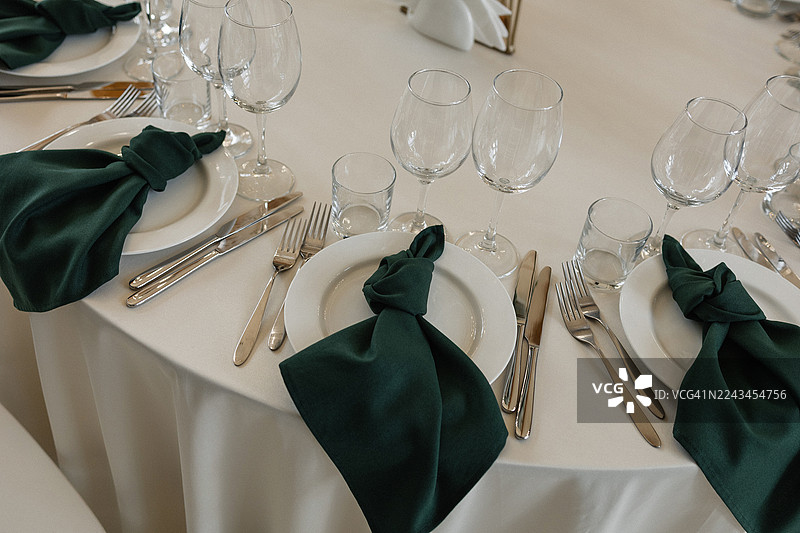 优雅的餐桌布置，白色的餐盘，深绿色的餐巾，铺在白色的桌布上图片素材