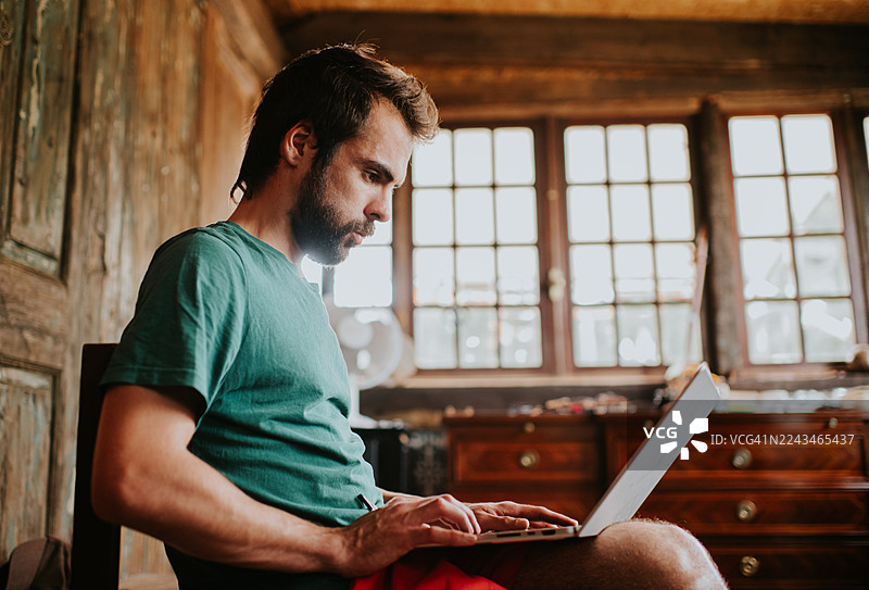 身穿绿色衬衫的男子在光线温暖的木屋里用笔记本电脑工作图片素材