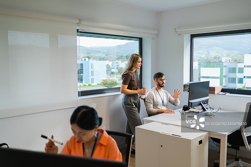 一群来自不同背景的商业专业人士在现代办公室的电脑前协作，讨论项目策略。图片素材