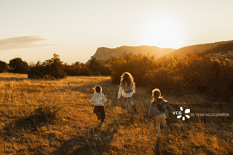 夕阳下，三个孩子奔跑在金色的田野上，温馨的户外家庭时刻图片素材