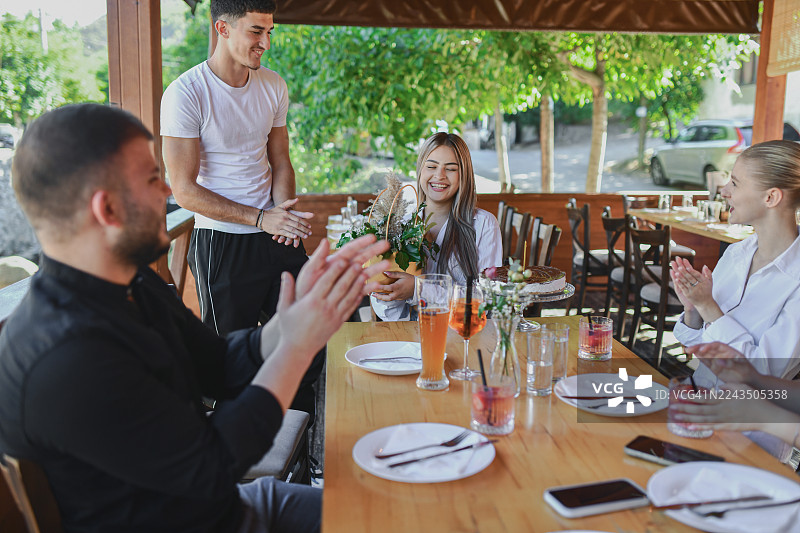 朋友们在户外餐厅庆祝生日，服务员献上鲜花和蛋糕图片素材