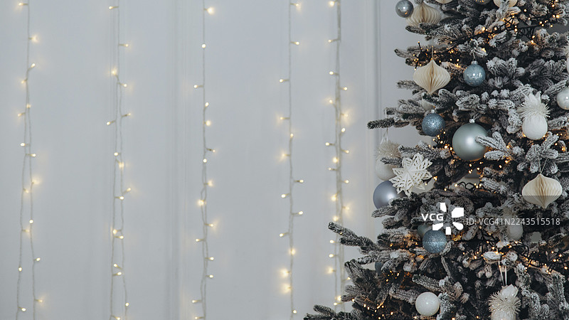 一棵华丽的植绒圣诞树矗立在墙边，墙上装饰着垂直的闪亮仙女灯串。图片素材