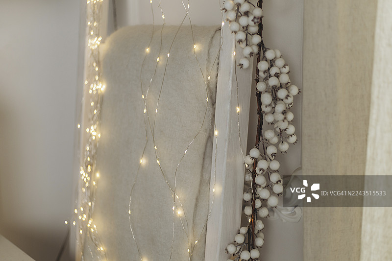 带软毯的梯子装饰着LED灯串和白色浆果花环。图片素材