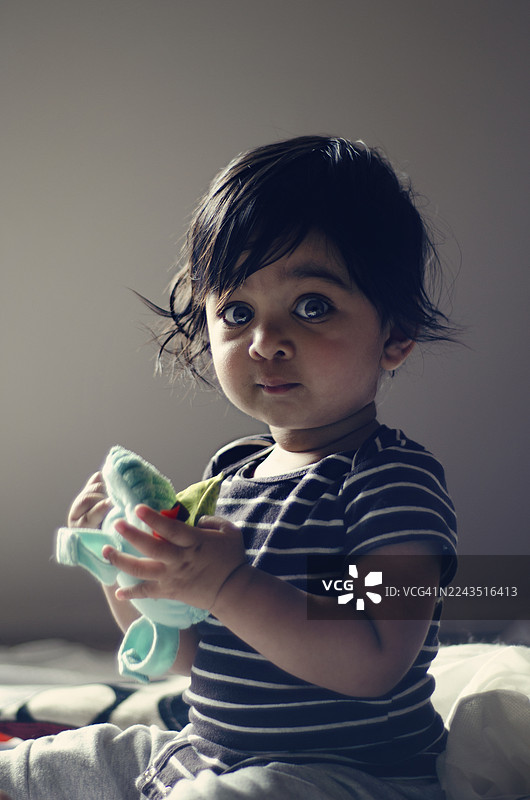 直接凝视：一个警觉的幼儿拿着玩具，表情好奇。一位印度男童的特写肖像。图片素材
