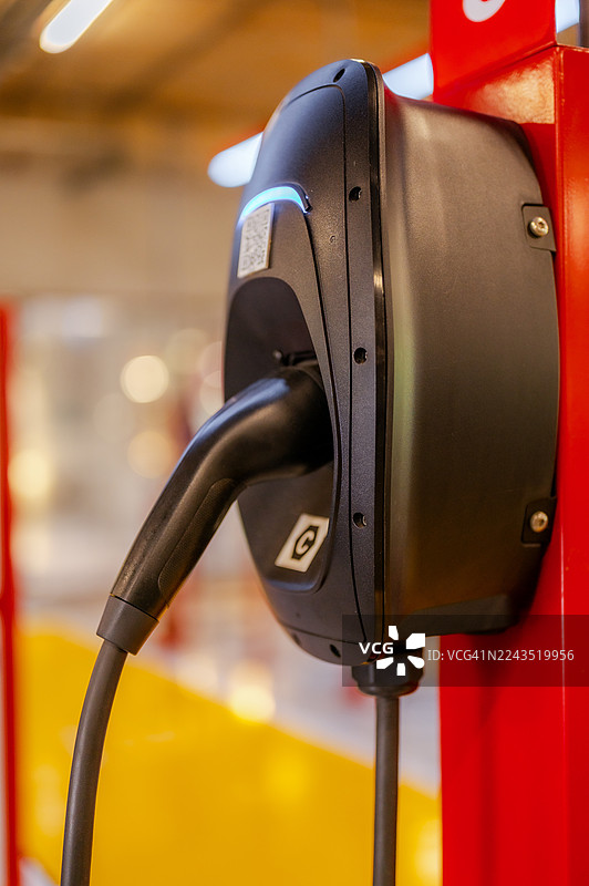 在公共停车场，于插电式充电站为您的电动汽车电池充电。清洁能源汽车，倡导绿色生活。图片素材