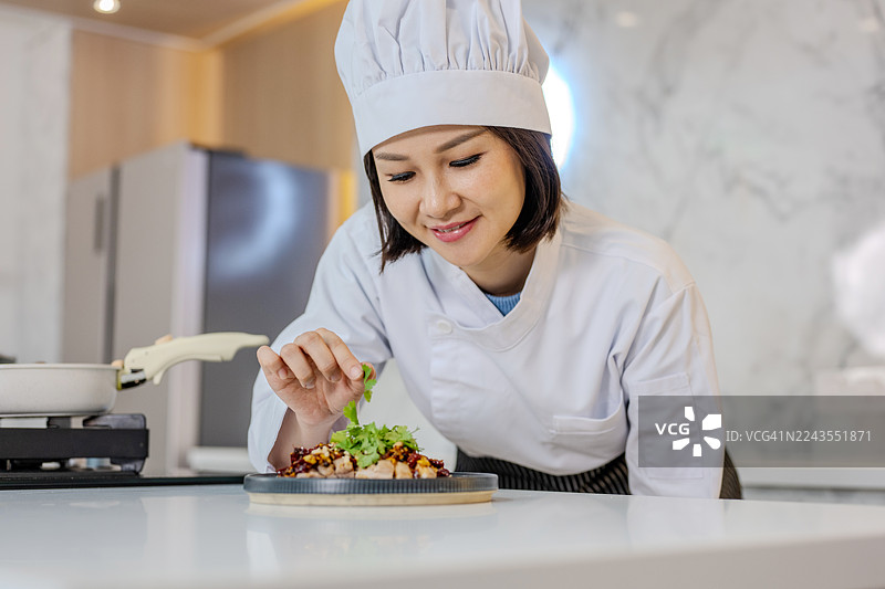 一位亚洲中国女厨师在商业厨房准备上菜，正在为一道辣子鸡最后的装饰。图片素材