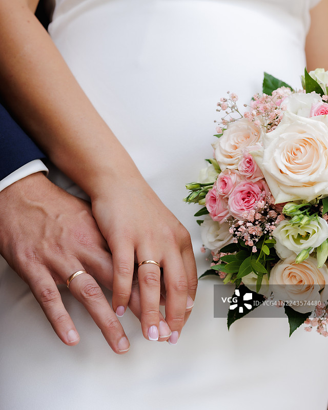 新郎新娘的双手戴着婚戒，背景是白色婚纱图片素材