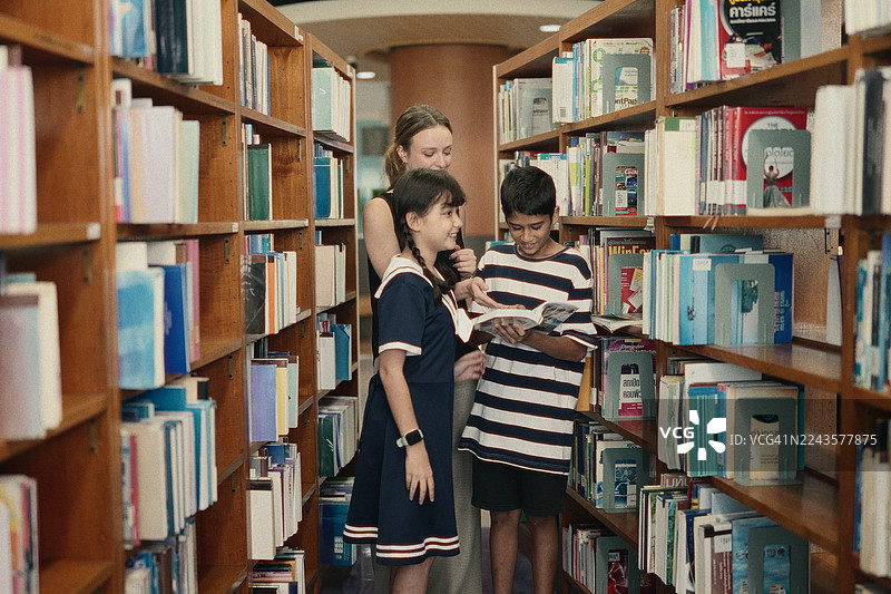 亚洲小学生和老师在学习时间一起在学校图书馆挑选要读的书。图片素材