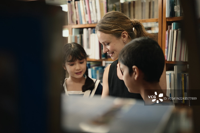 在明亮的教室图书馆里，一位老师指导着年轻的亚洲学生选择学习书籍。图片素材