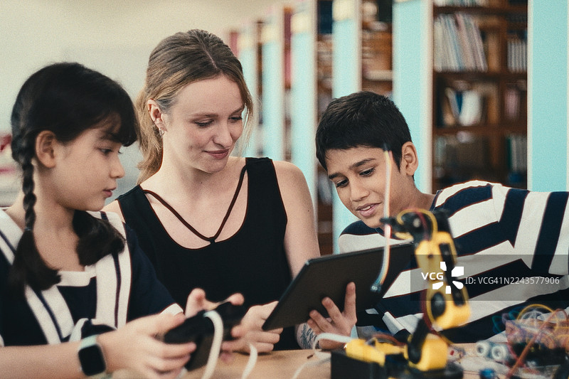 学生们围在女老师身边，她在科学教室里讲解机械臂的功能，学生们正在学习自动化知识。图片素材