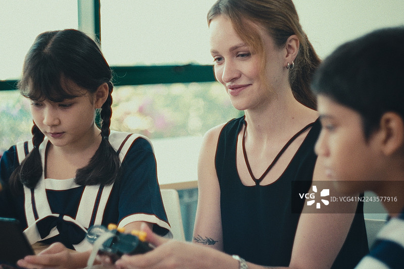 学生们围着女老师，在科学教室里学习自动化，了解机器人手臂的功能。图片素材