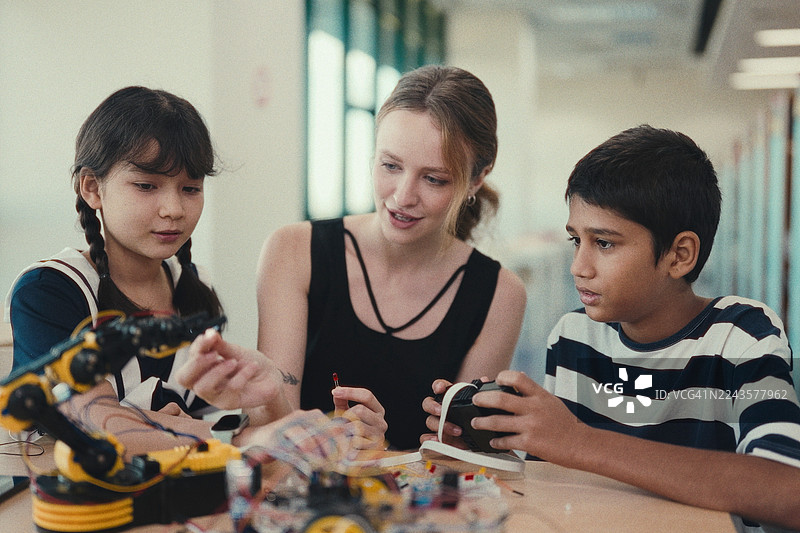 一位女老师在现代科学教室里指导一群学生学习机器人手臂。图片素材