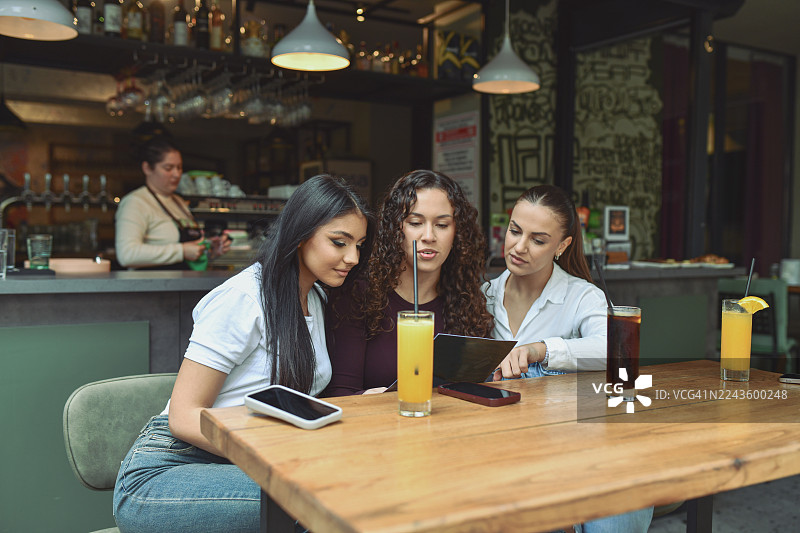 三位朋友在舒适的酒廊吧台桌旁分享饮品，边看菜单边喝鲜榨果汁。图片素材