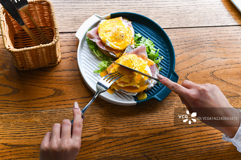 烤面包上卧着荷包蛋的早午餐拼盘，在餐桌上被手切开图片素材