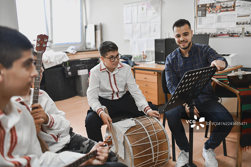 一位老师在传统音乐课上，指向乐谱指导年轻的学生。图片素材