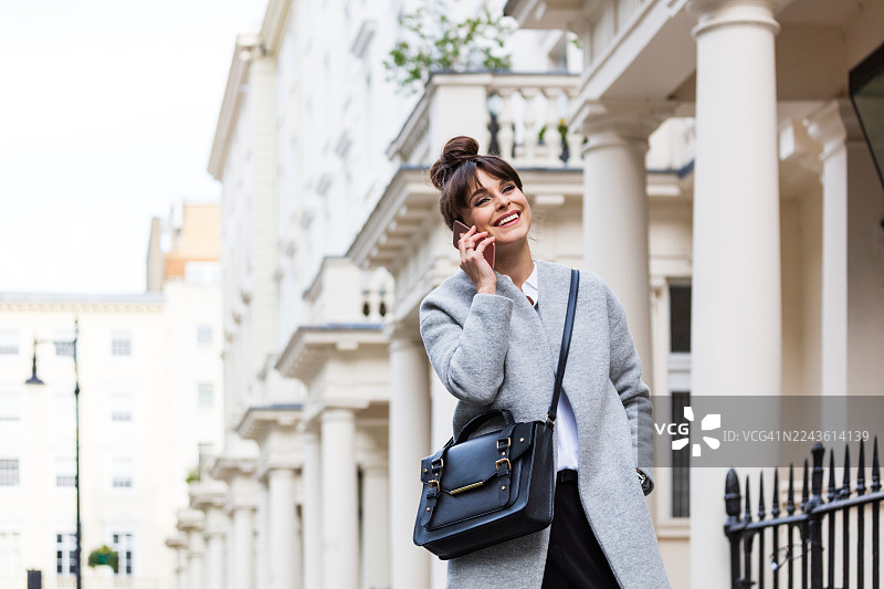 优雅美丽的女人在城市房屋前打电话图片素材