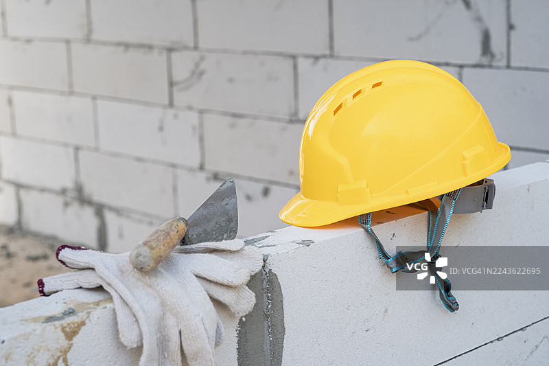 在施工期间，安全帽、抹子和手套放在砌块墙上，展示了建筑工作的必需品。图片素材