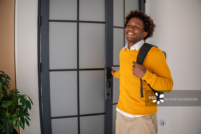 自信的黑人年轻商务人士背着背包，面带微笑步入现代办公室，准备开始重要的一天图片素材