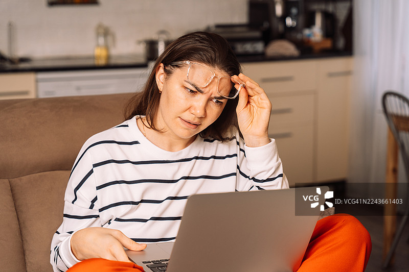 一位女士微笑着，一边咬着眼镜，一边看着笔记本电脑图片素材