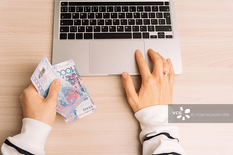 笔记本电脑旁的手拿着十坚戈纸币图片素材