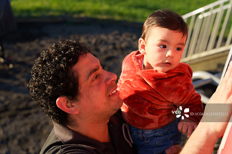 拉丁美洲的父亲在户外抱着戴着助听器的儿子图片素材