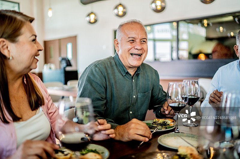 一位年长的男士在餐厅与朋友们共进晚餐时交谈图片素材