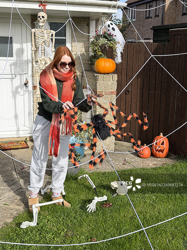 女孩装饰房屋和花园以迎接万圣节/诡异的蜘蛛网、南瓜、骷髅和蜘蛛，秋季节日欢乐图片素材