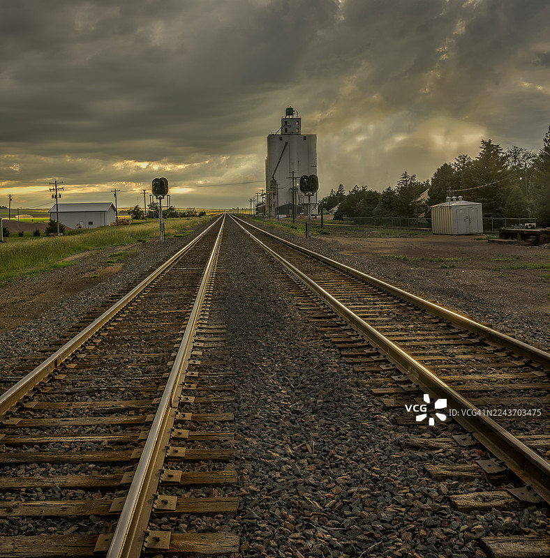 大平原上日落时分戏剧性的天空，伴随着谷物仓储和火车轨道图片素材