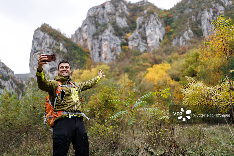 一个男人独自在美丽的秋日大自然中徒步，用智能手机自拍，脸上带着笑容图片素材