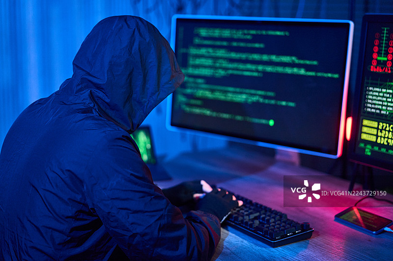在黑暗的房间里，一名黑客正在电脑上敲打代码图片素材