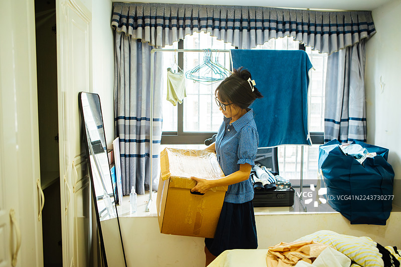 搬家当天，一位年轻亚洲女性正在整理房间，她手里拿着一个纸箱，展现出生活方式、居家搬迁的积极能量和崭新开始。图片素材