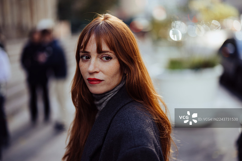 姜黄色头发的女性在城市街道上，城市晚间光线下的沉思肖像图片素材