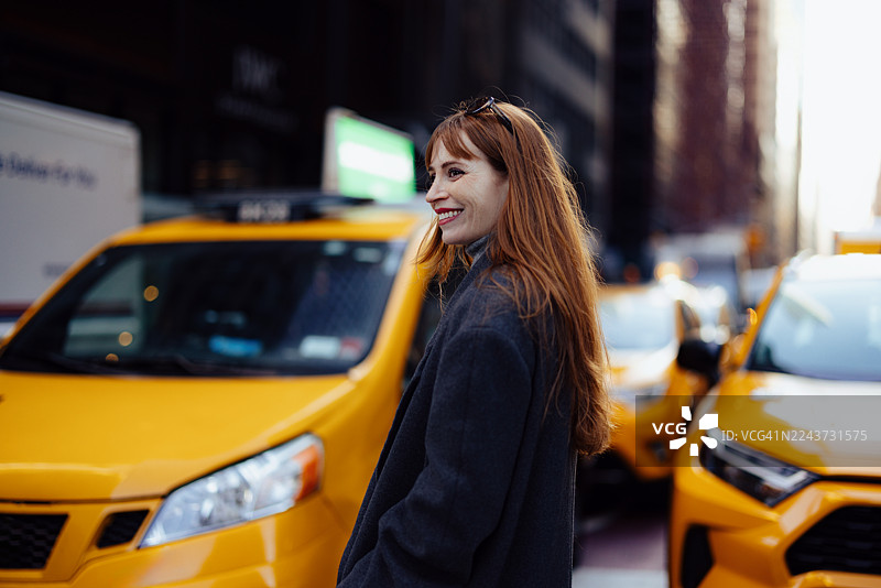 纽约街头，身处黄色出租车之间，一位红发女子面带微笑，繁忙都市街景中的城市肖像图片素材