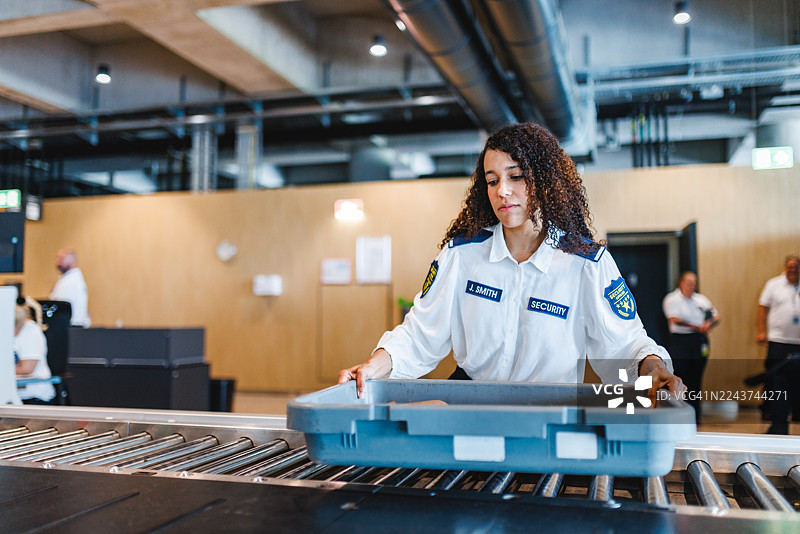 专注的年轻西班牙裔女性机场安检人员在室内操作行李安检系统图片素材