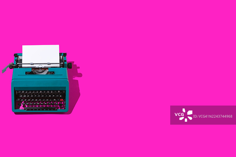 绿色的复古打字机，带有空白页，位于左侧，背景为紫红色。编剧、作家、写作、新闻、文学和文化。图片素材