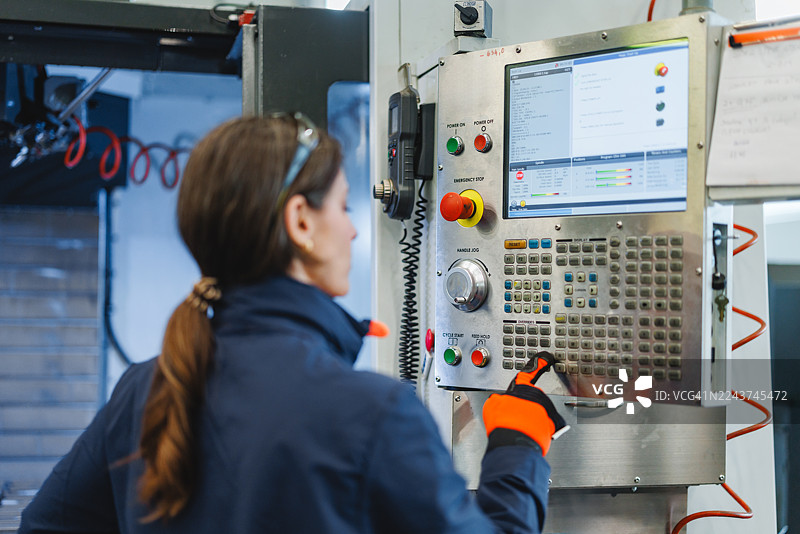 专注的中年白种女性在工业车间操作数控机床控制面板图片素材