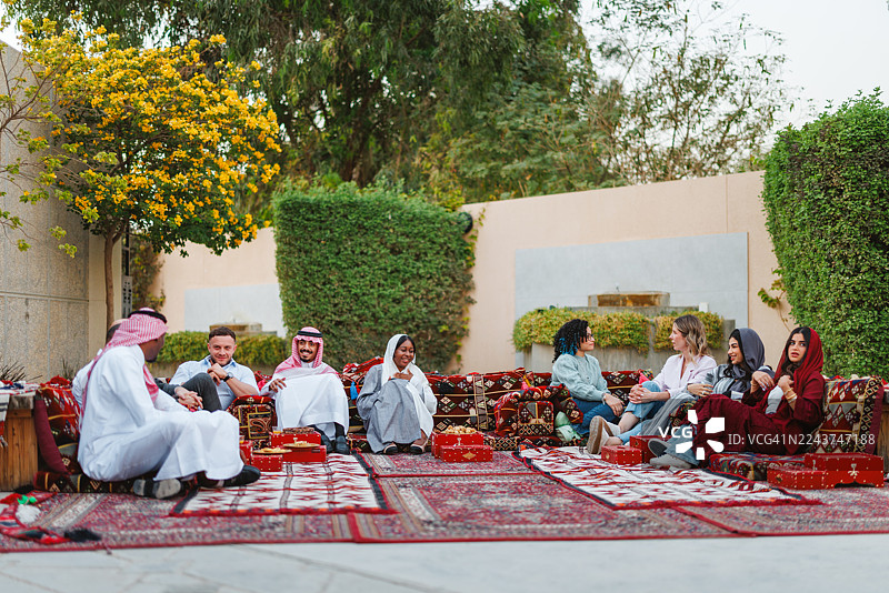 不同背景的中东成年人在庭院里围坐垫子愉快地交谈图片素材