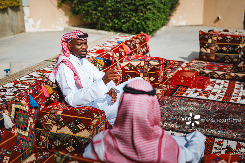 身着传统服饰的中东男子在户外马吉利斯聚会中交谈图片素材
